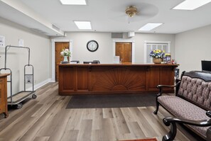 A reception area with a wooden reception desk, a clock, a bench, and a cart.