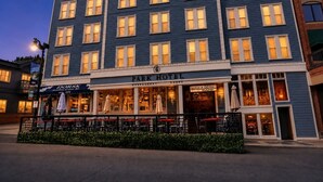 Un edificio de varios pisos con restaurante y tiendas en la planta baja, un letrero de estacionamiento y mesas al aire libre.