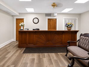 Zona de recepción con un mostrador de madera, un reloj y una silla.