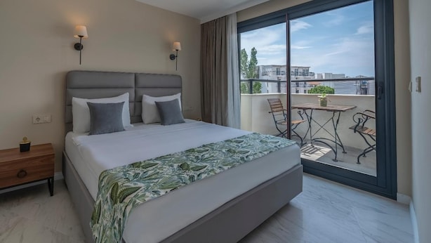 Ett modernt hotellrum med en stor säng, två sänglampor, en balkong med bord och stolar samt utsikt över staden.