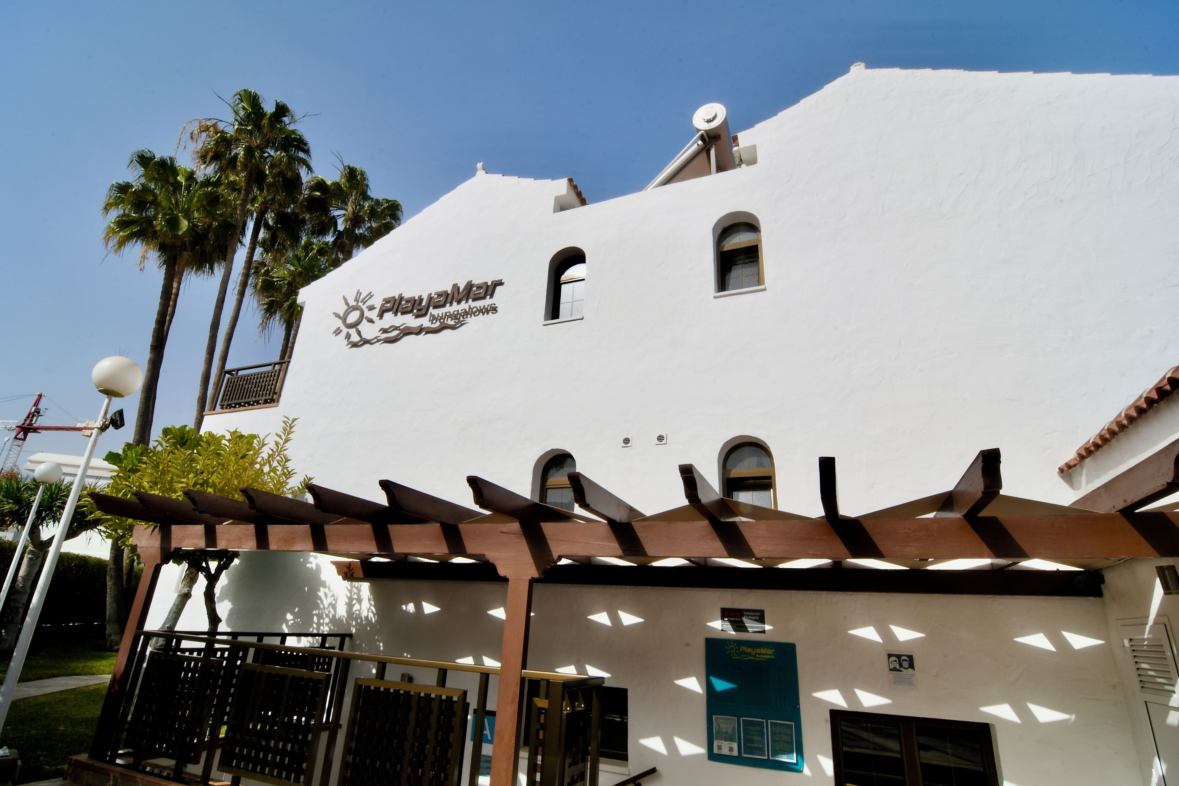 A white building with a sign for 'Playamar Bungalows' and a pergola structure in front.