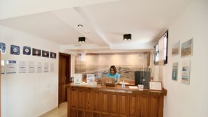 A reception desk with a wooden finish, a person seated behind it, and various framed certificates on the walls. - Bungalows Playamar (San Bartolomé de Tirajana)