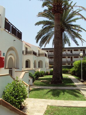 Une cour avec un palmier, un bâtiment doté de balcons et un ciel dégagé.