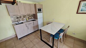 Eine kompakte Küche mit Spüle, Mikrowelle und kleinem Kühlschrank. Ein Esstisch mit Stühlen steht bereit.