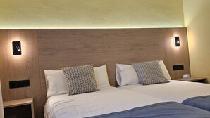 A hotel room with a wooden headboard, two beds with blue bedding, and bedside lamps. - Bungalows Playamar (San Bartolomé de Tirajana)