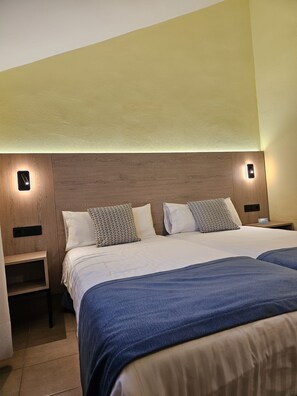 Ein Hotelzimmer mit einem hölzernen Kopfstück, zwei Betten mit blauer Bettwäsche und Nachttischlampen.