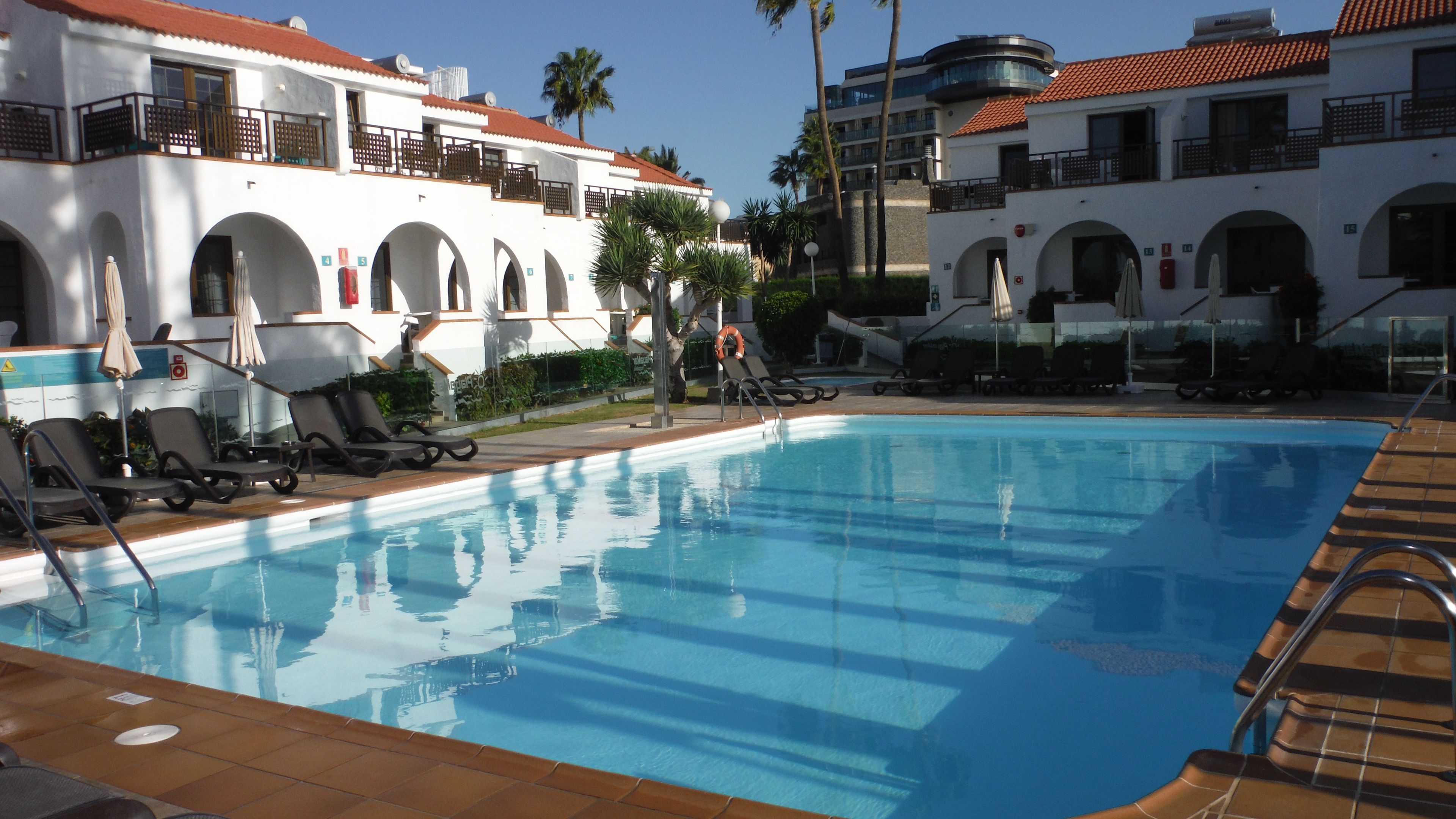A swimming pool with lounge chairs and umbrellas, surrounded by buildings with arched windows and balconies.