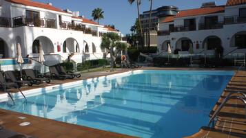 A swimming pool with lounge chairs and umbrellas, surrounded by buildings with arched windows and balconies.