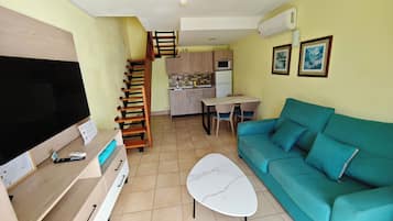 A living room with a TV, sofa, coffee table, and a staircase leading to a kitchen.