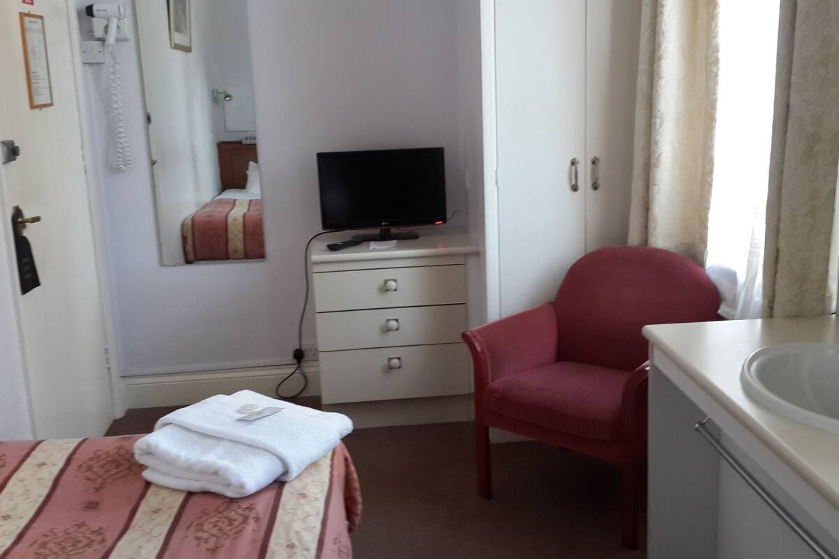 A hotel room with a bed, a red chair, a TV on a dresser, a mirror, and a sink.