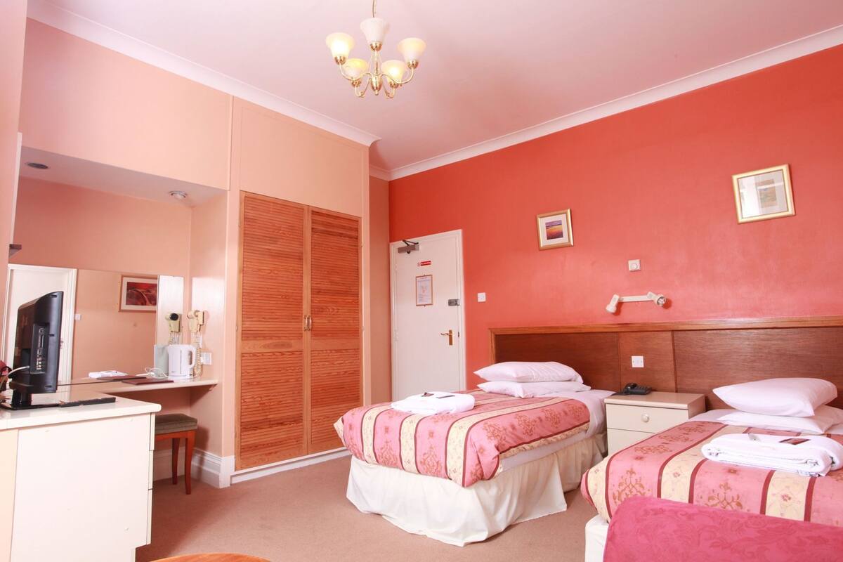 A hotel room with two beds, a desk with a computer, a wardrobe, and a shower area.