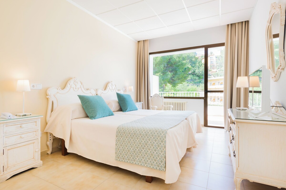 A spacious bedroom with a large bed, a dresser, and a view of the outdoors.