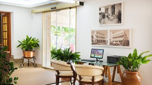 Una habitación con escritorio, dos sillas, ordenador y plantas en macetas.