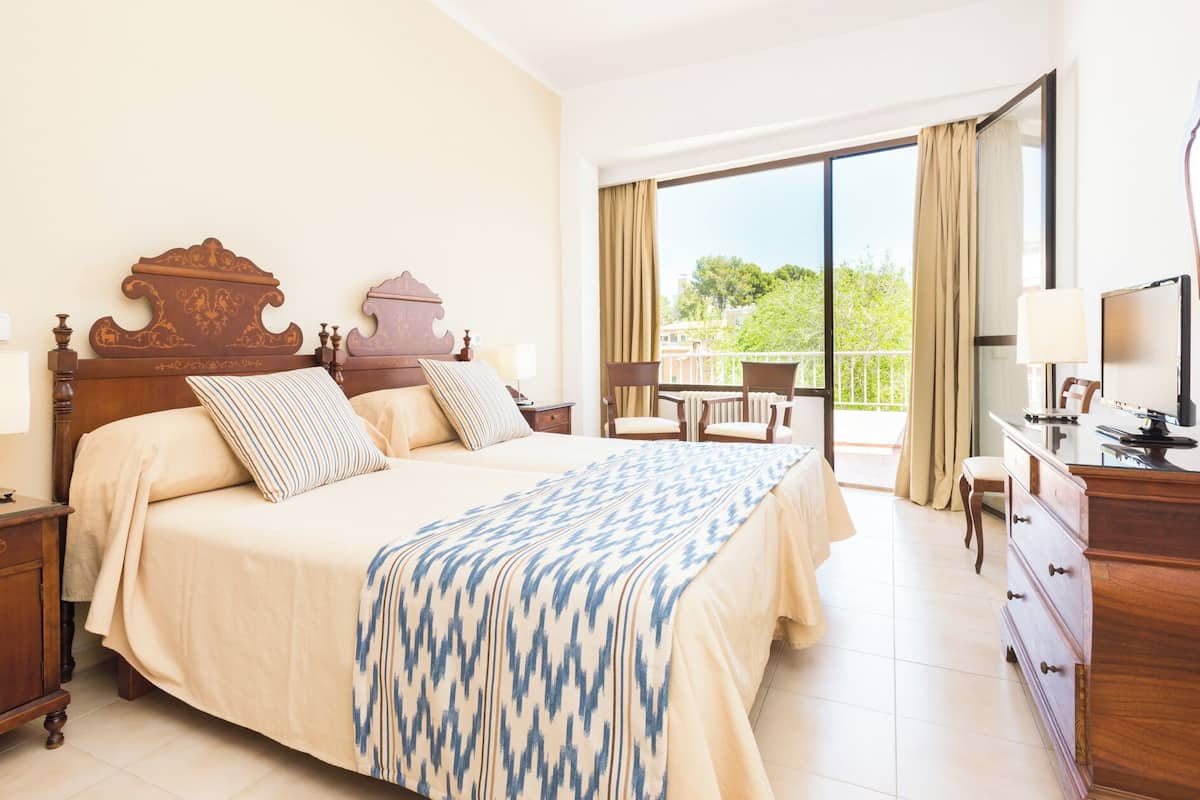 A hotel room with a large bed, a desk with a computer, a chair, and a balcony with a view.