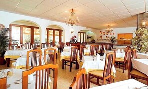 A dining area with multiple tables and chairs, a chandelier, and a bar area. - Gaya (Calvia)