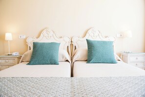 Una cama doble con cabecera blanca y dos almohadas turquesa, una mesita de noche con lámpara y un mueble auxiliar con un teléfono.