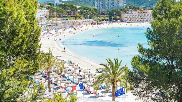 Una playa con sombrillas, gente y edificios al fondo.
