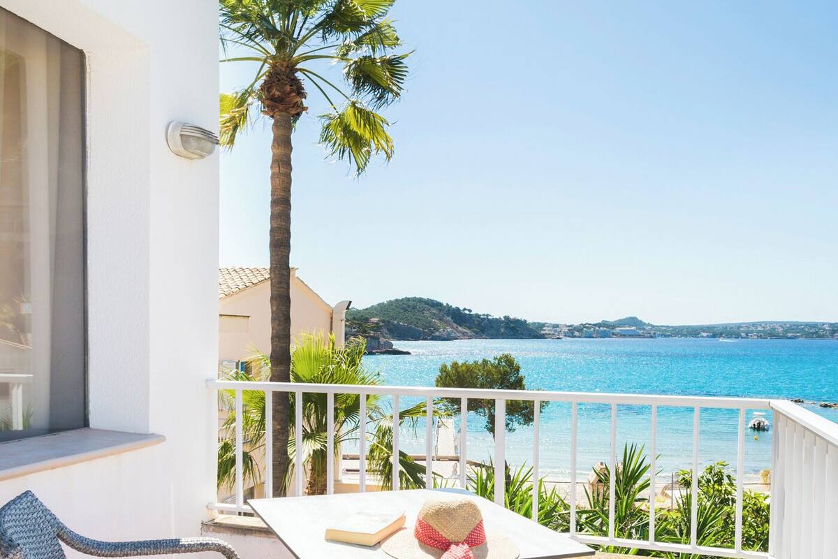 Un balcon avec des fauteuils en osier, une table et une vue sur la mer.