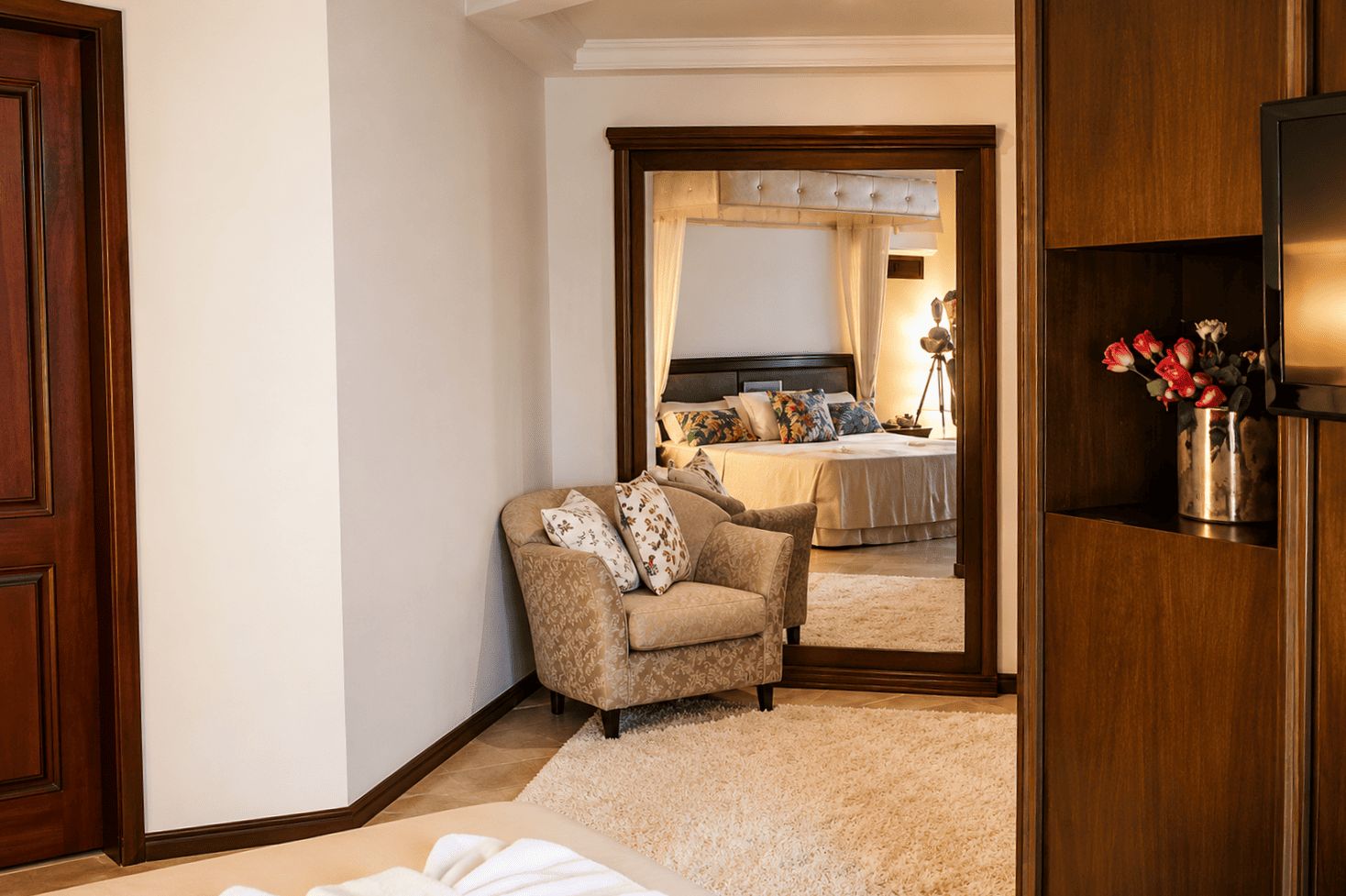 Un dormitorio con un espejo grande, un sofá, una cama y un armario de madera con un jarrón de flores.