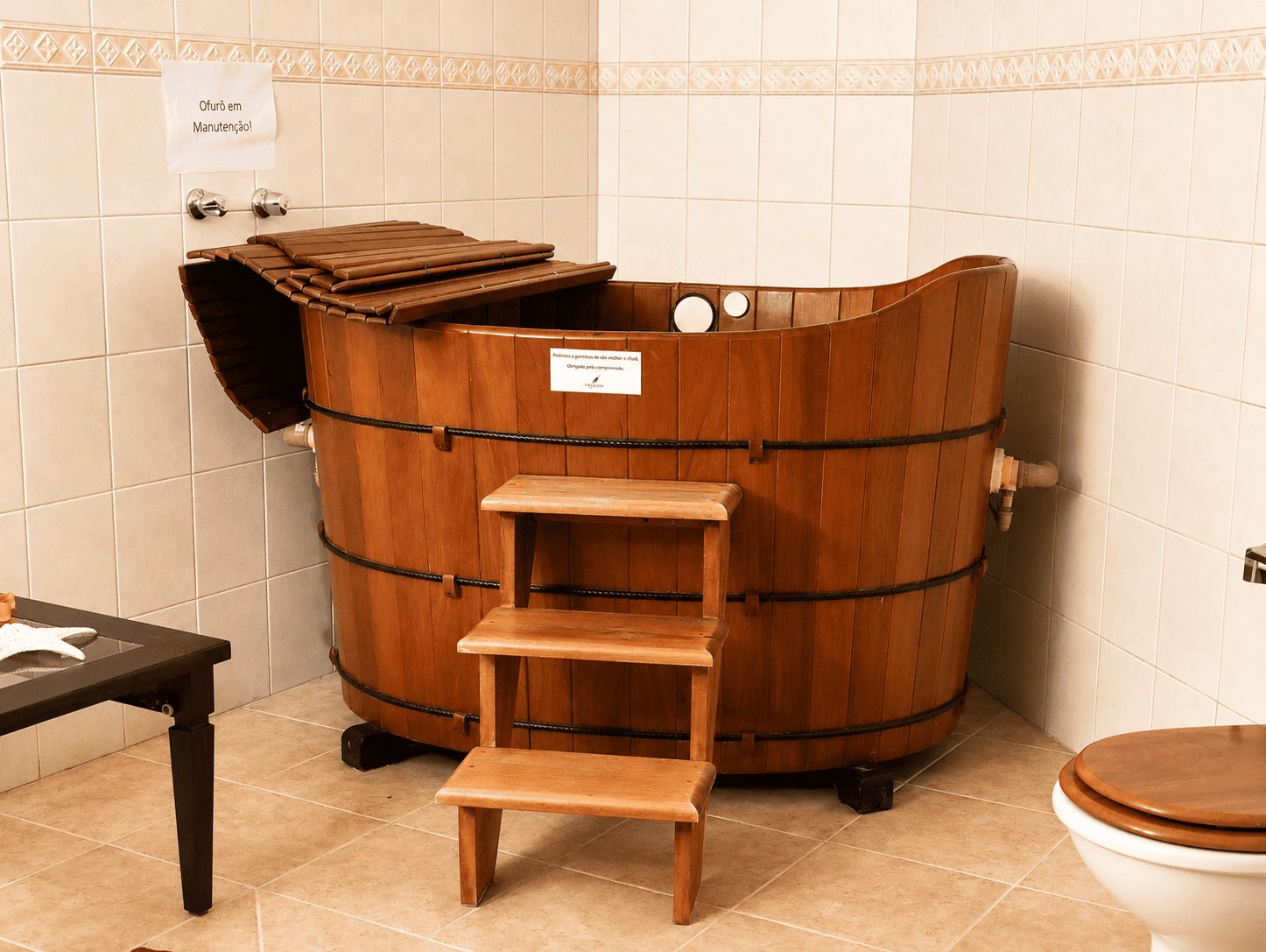 Una vasca da bagno in legno con uno sgabello di legno, in un bagno con pareti piastrellate e un water.