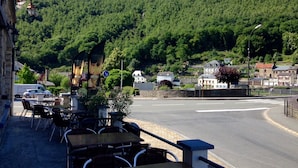 A street view with a café, tables, chairs, and a mountain in the background. - Hôtel les Boucles de Meuse (Montherme)