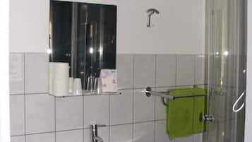 Une salle de bain avec un lavabo blanc, un miroir, une cabine de douche en verre et une serviette verte suspendue à un porte-serviettes.