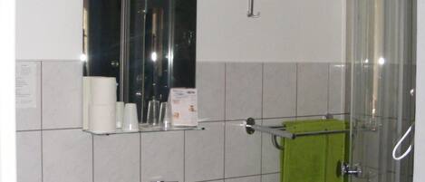 A bathroom with a white sink, a mirror, a glass shower enclosure, and a green towel hanging on a rack.