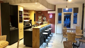 A bar area with stools, a counter, and a kitchen in the background. - Hôtel les Boucles de Meuse (Montherme)