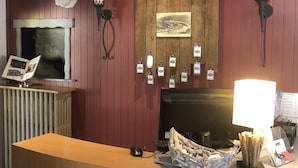 A reception desk with a wooden counter, a computer, and a decorative wall with plaques and a framed picture. - Hôtel les Boucles de Meuse (Montherme)