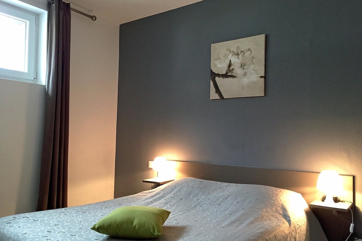 Ein Schlafzimmer mit einem Bett, einem grünen Kopfkissen, einem Wandbild und Nachttischlampen.