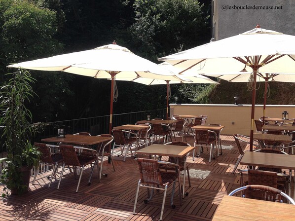 An outdoor patio with wooden tables and chairs, covered by large umbrellas.