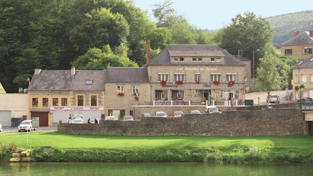 A building with a restaurant and hotel on the ground floor, a stone wall in front, and a river in the foreground. - Hôtel les Boucles de Meuse (Montherme)