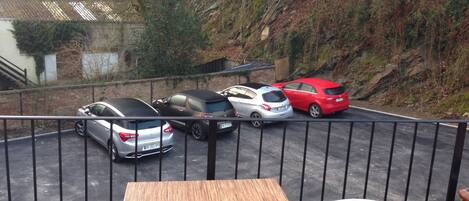 A balcony with a table and chairs overlooking a parking area with several cars.