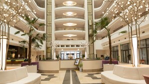 A spacious lobby with a central reception desk, multiple seating areas, and a high ceiling with circular lighting fixtures. - Mövenpick Samarkand (Samarkand)