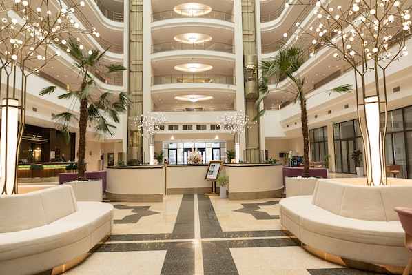 A spacious lobby with a central reception desk, multiple seating areas, and a high ceiling with circular lighting fixtures. - Mövenpick Samarkand (Samarkand)