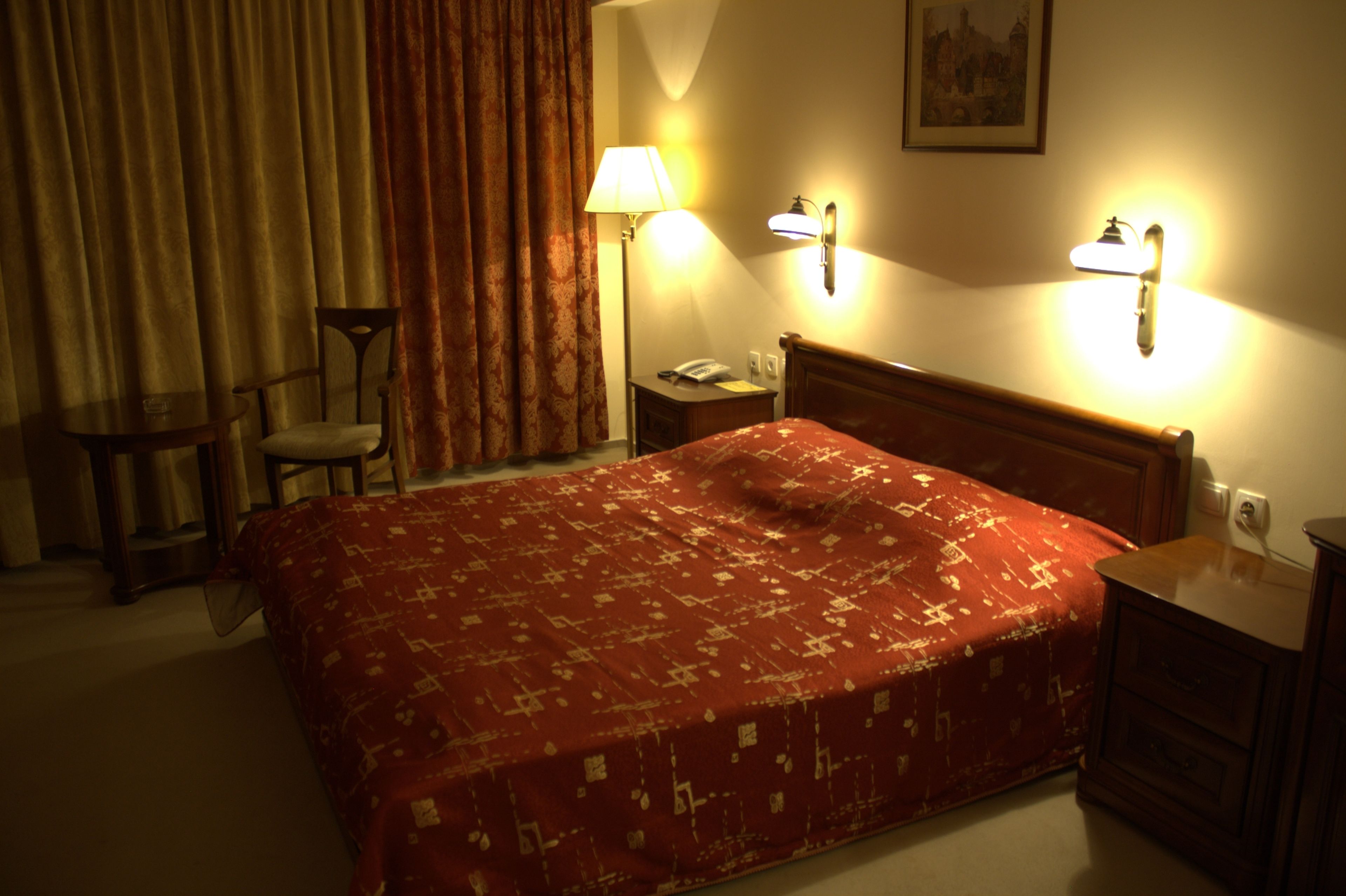 A hotel room with a large bed, a nightstand, a lamp, and a chair.