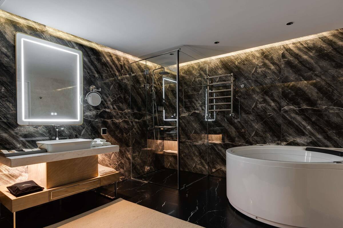 A modern bathroom with a large mirror, two sinks, a glass-enclosed shower, and a freestanding bathtub.