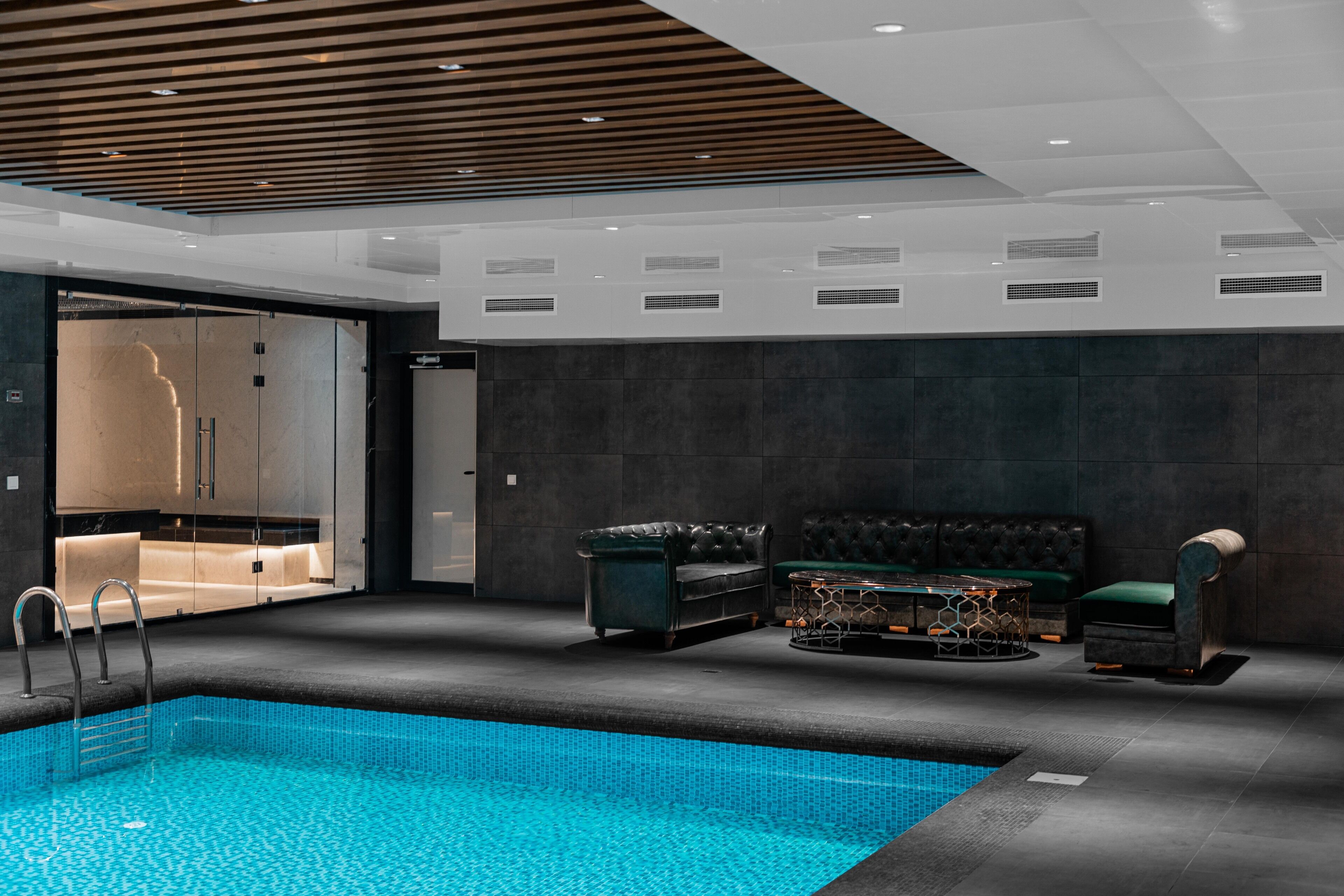 A modern indoor pool area with a clear pool, dark-toned seating, and recessed lighting.