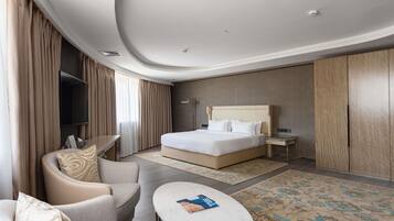 A modern hotel room with a large bed, a desk, a sofa, and a small table.