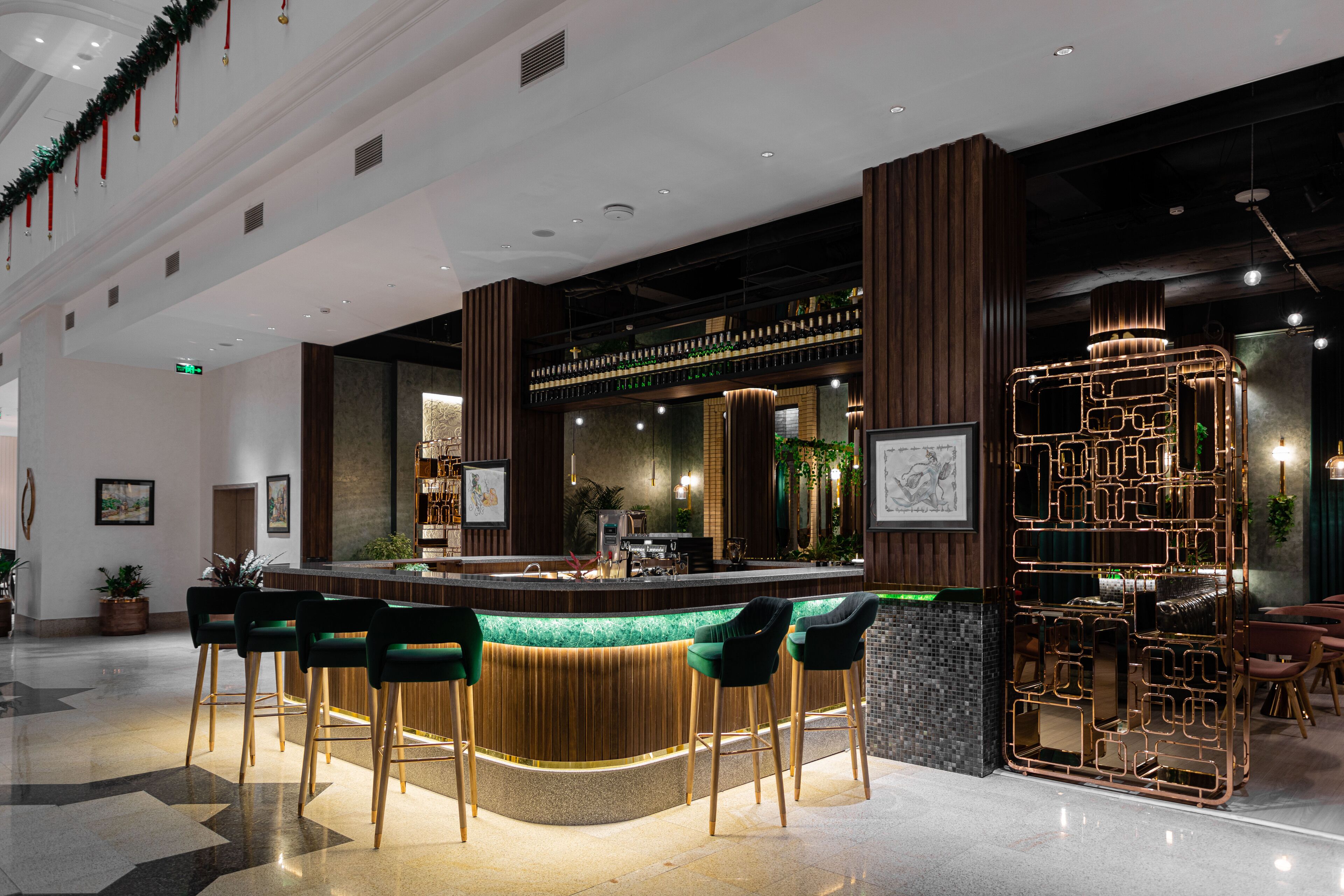Een moderne bar met een gebogen toonbank, groene barkrukken en een decoratieve metalen scheiding.