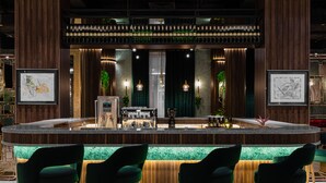 A bar area with a wooden bar counter, green bar stools, and framed artwork on the walls. - Mövenpick Samarkand (Samarkand)