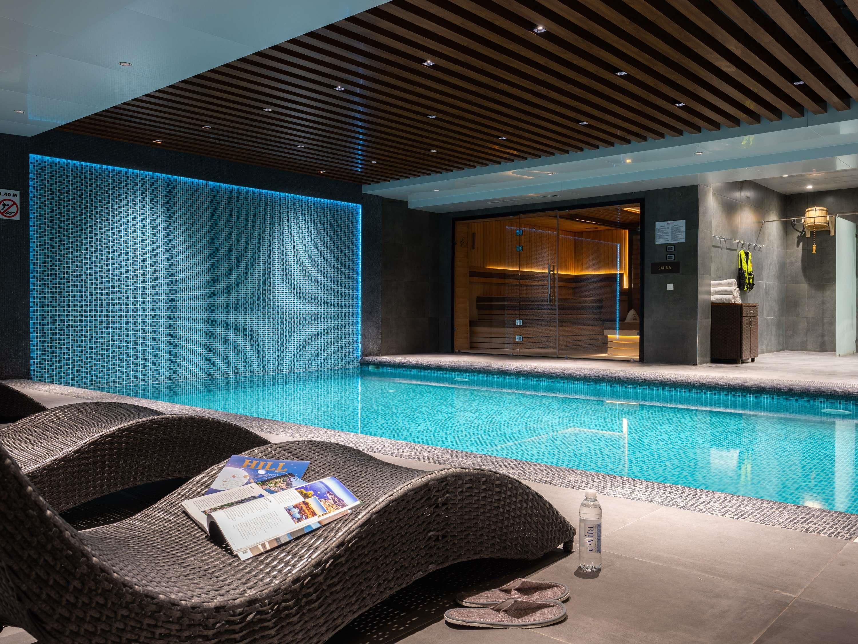 Un espace piscine intérieur moderne offrant une vue dégagée sur le bassin, des chaises longues et un espace sauna.
