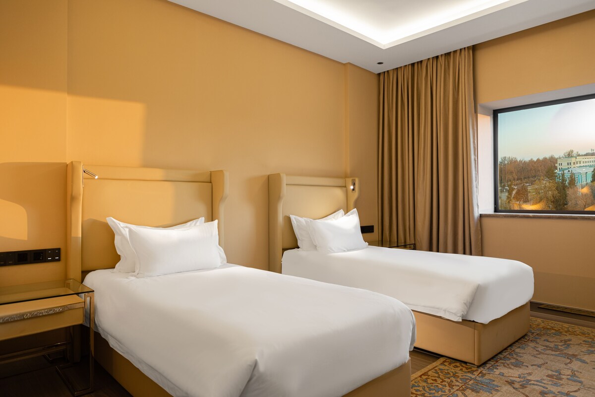A hotel room with two beds, a large window with a view, and a modern design.