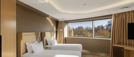 A hotel room with a large bed, a desk, a TV, and a window with curtains.