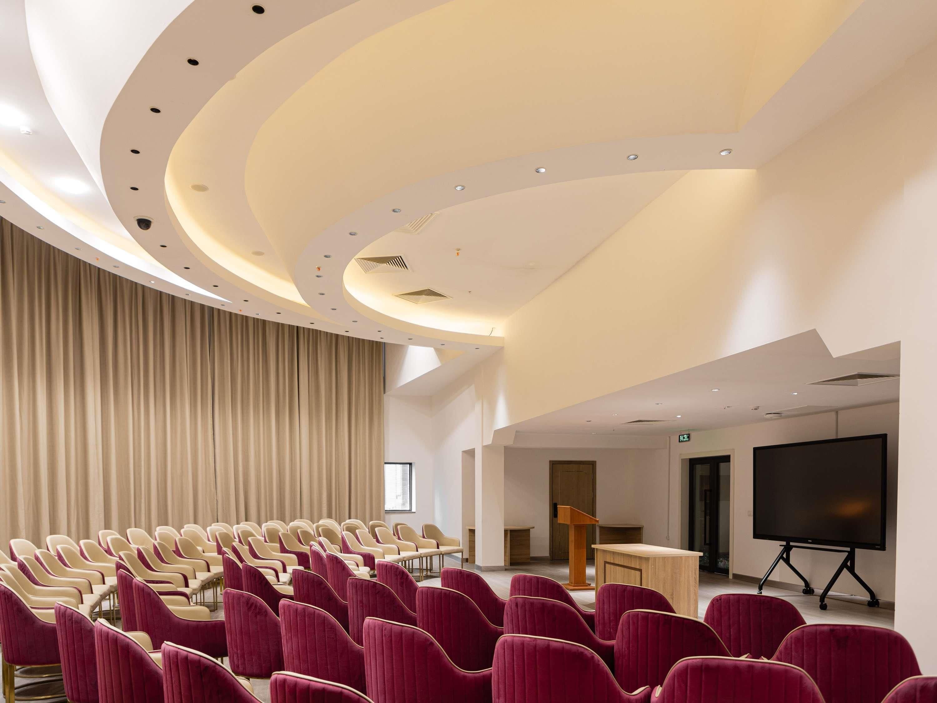 A conference room with rows of chairs, a podium, a large screen, and a curved ceiling.