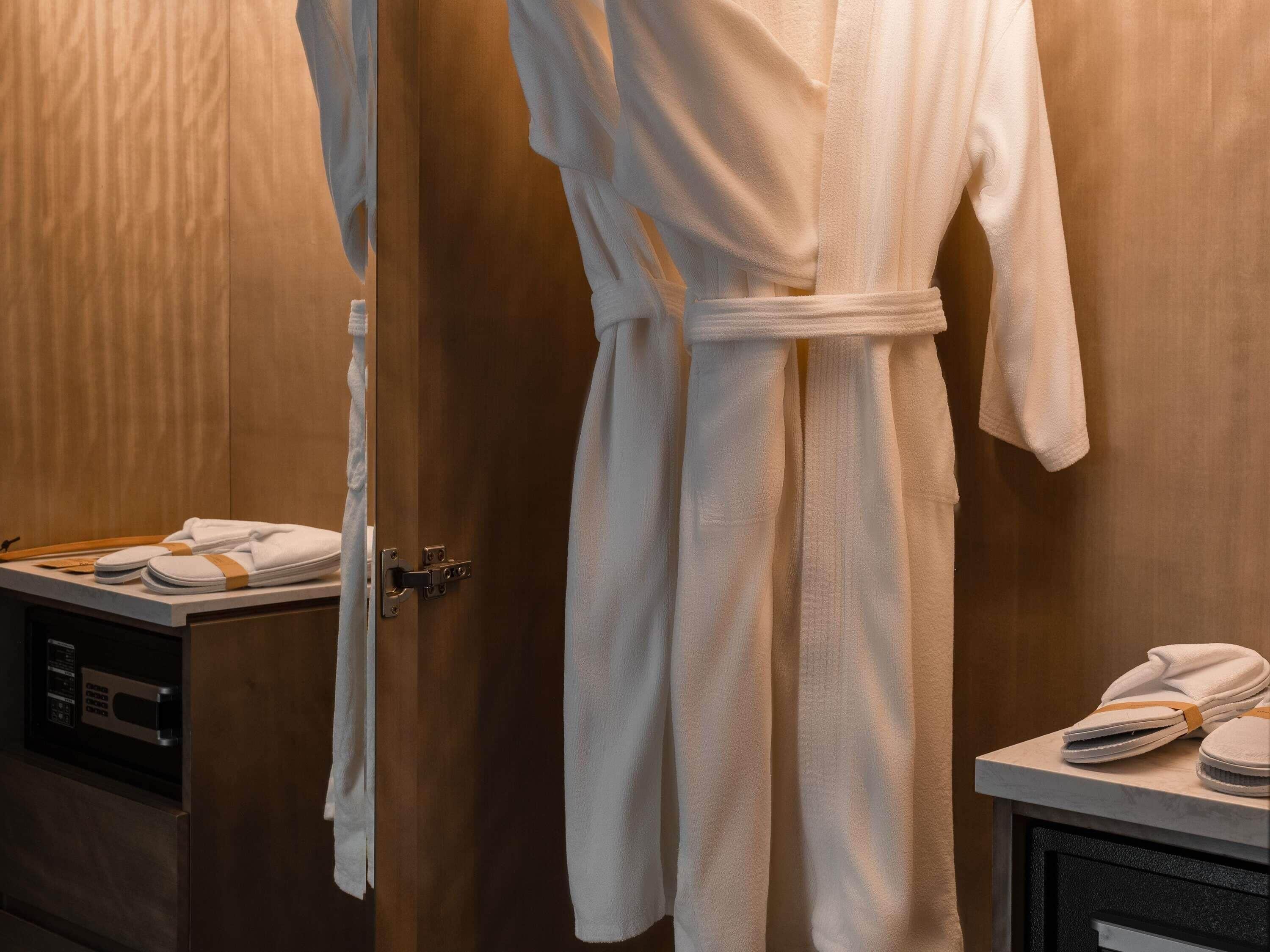 A bathroom with a wooden wall, a white robe hanging on a door, and a towel rack with folded towels.