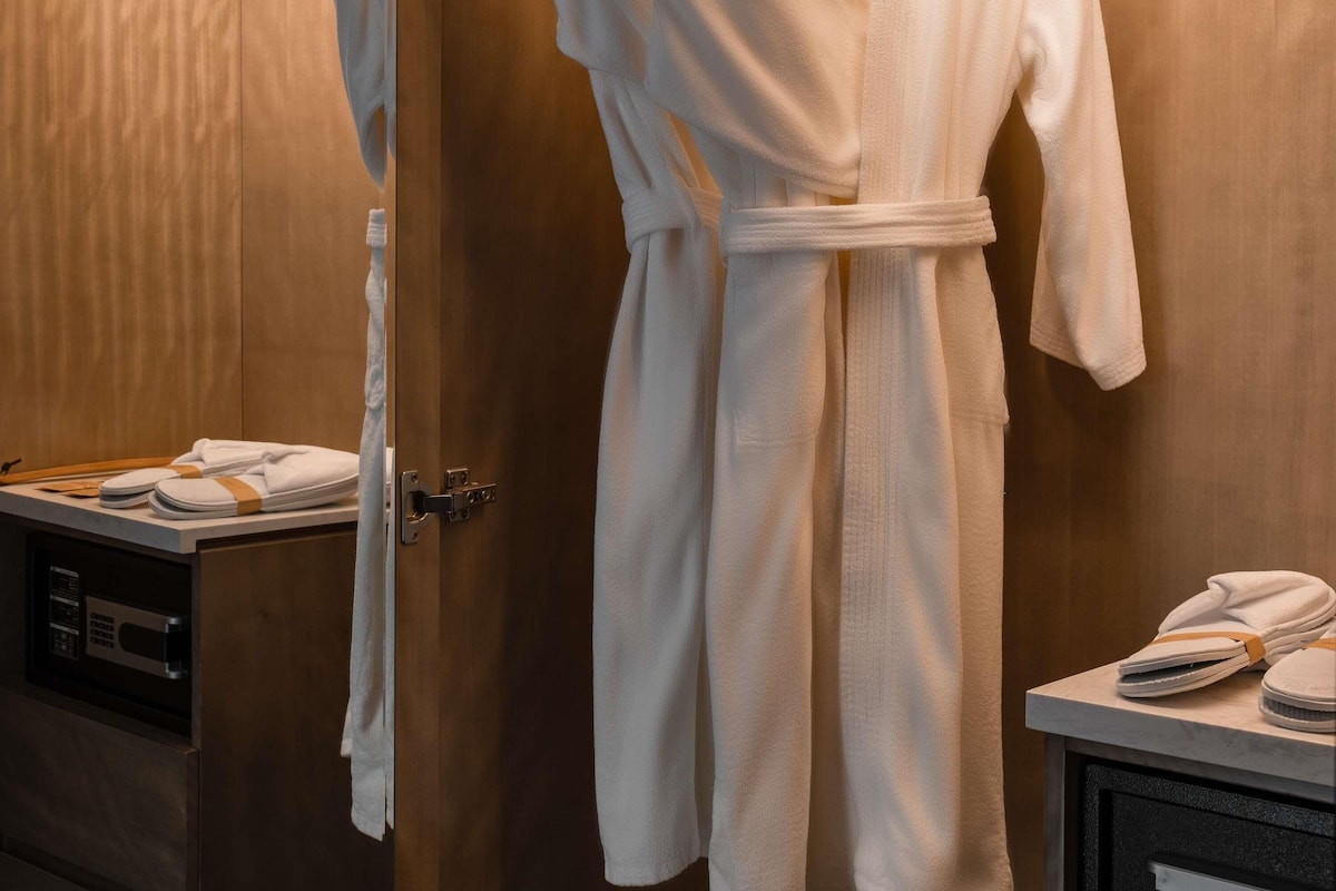 A bathroom with a wooden wall, a white robe hanging on a door, and a towel rack with folded towels.