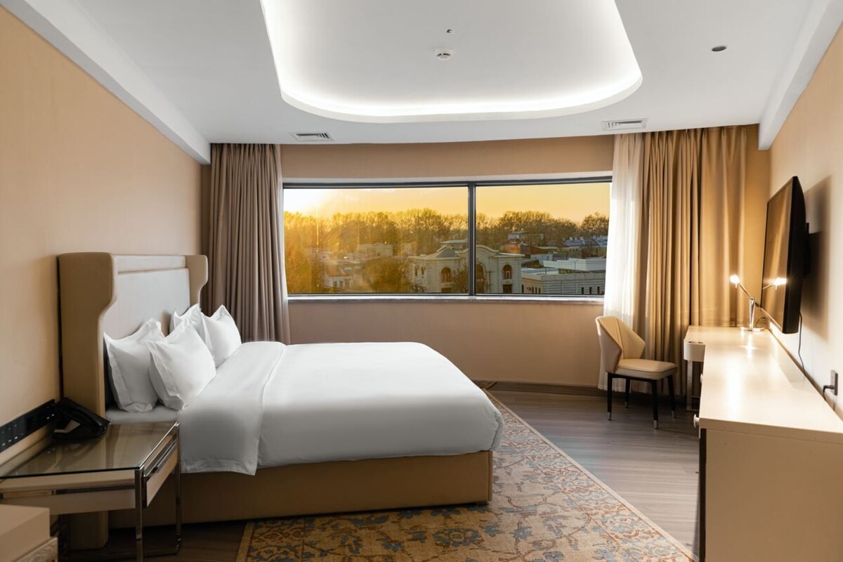 A modern hotel room with a large bed, a desk, a chair, and a television.