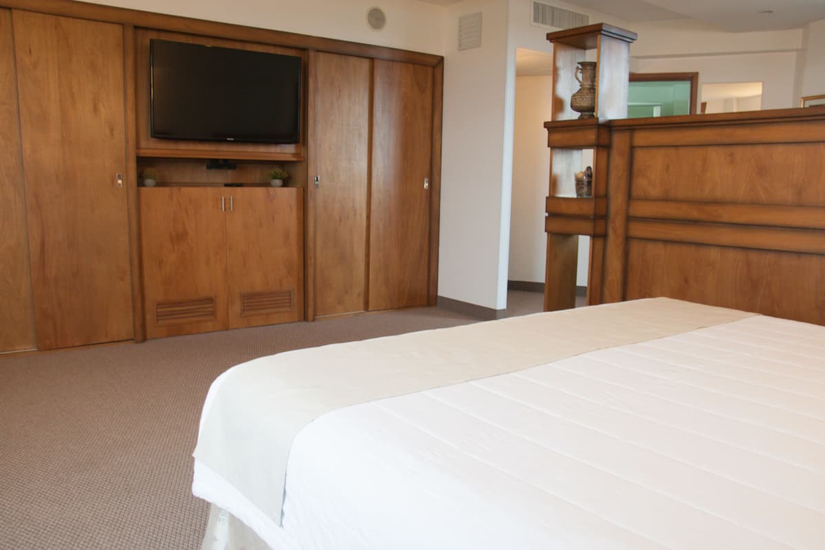 A hotel room with a large bed, wooden wardrobe, and a television mounted on the wardrobe.