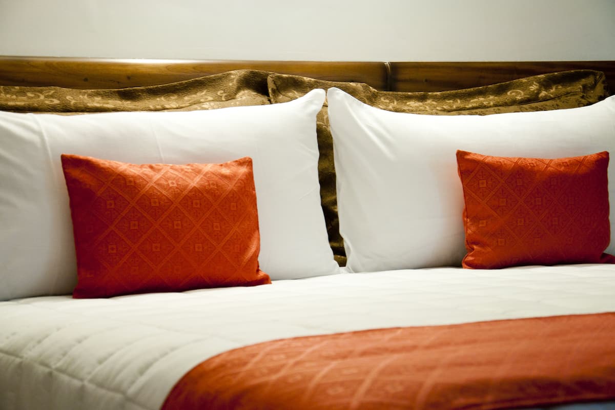 A bed with white and orange pillows, a wooden headboard, and a white bedspread.